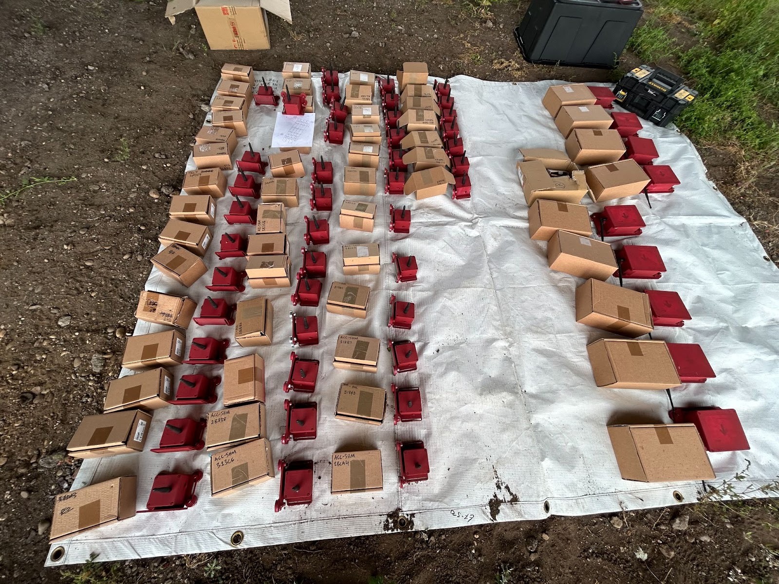 Display of large quantity of specialized equipment laid out on a white tarp in a field, which appears consistent with technical monitoring devices.